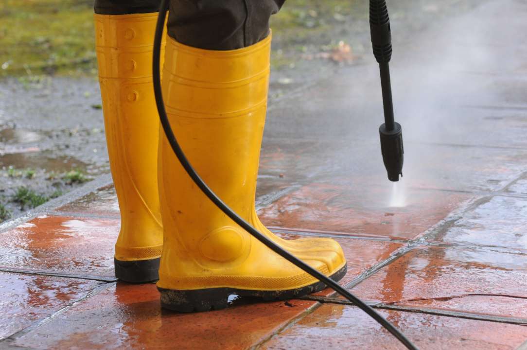 person wearing yellow rubber boots with high pressure water nozzle cleaning patio